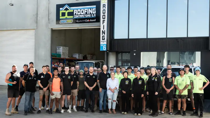 DC Roofing Contractors SA team standing outside the company's warehouse and office building in front of work vehicles.